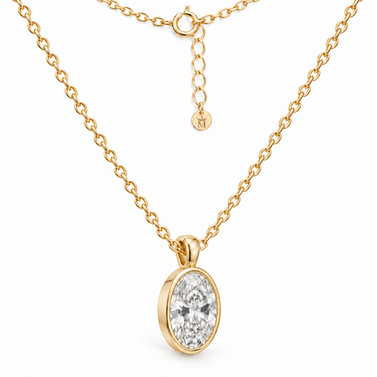 Three-quarter view of the oval lab-grown diamond bezel pendant and 14K gold chain. AI-edited crown-M engraving concept on the existing extender end disc; engraving and scale are illustrative.
