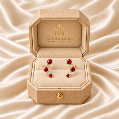 MISSISSI Scarlet Arc lab-grown ruby stud earrings in yellow gold, presented as a pair in champagne octagonal packaging with crown M branding; design visualization.