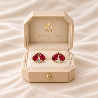 MISSISSI Scarlet Fold twin-pear lab-grown ruby stud earrings in yellow gold, presented as a pair in champagne octagonal packaging with crown M branding; design visualization.