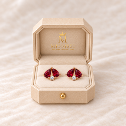 MISSISSI Scarlet Fold twin-pear lab-grown ruby stud earrings in rose gold, presented as a pair in champagne octagonal packaging with crown M branding; design visualization.