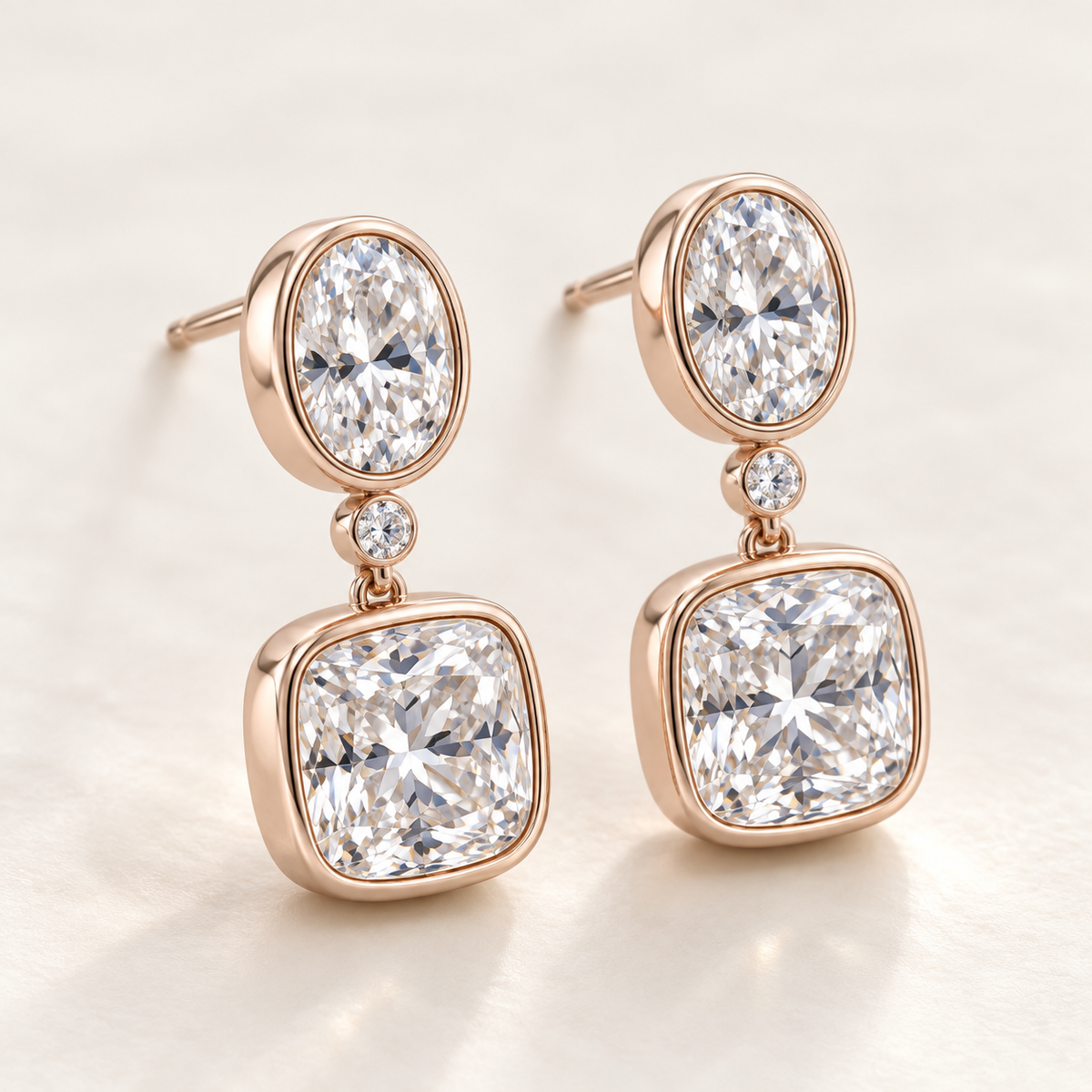 MISSISSI AA14 paired earrings in pale rose gold tone, three quarter view showing an oval diamond above one small round connector diamond and a cushion-shaped drop in rounded bezels; design visualization