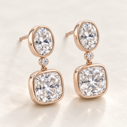 MISSISSI AA14 paired earrings in pale rose gold tone, three quarter view showing an oval diamond above one small round connector diamond and a cushion-shaped drop in rounded bezels; design visualization