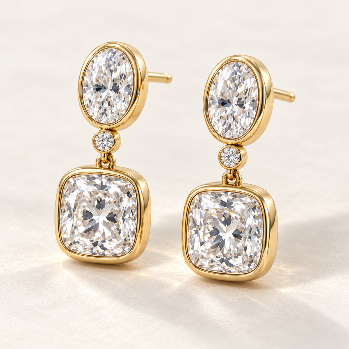 MISSISSI AA14 paired earrings in yellow gold tone, three quarter view showing an oval diamond above one small round connector diamond and a cushion-shaped drop in rounded bezels; design visualization