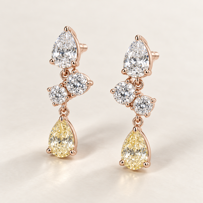 MISSISSI AA20 paired earrings in pale rose gold tone, three quarter view showing a white pear-shaped diamond above two diagonally arranged round diamonds and a pale-yellow pear-shaped drop; design visualization