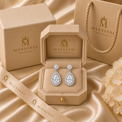 Cora pear halo drop earrings in 14K white gold, presented in coordinated champagne-beige MISSISSI packaging.