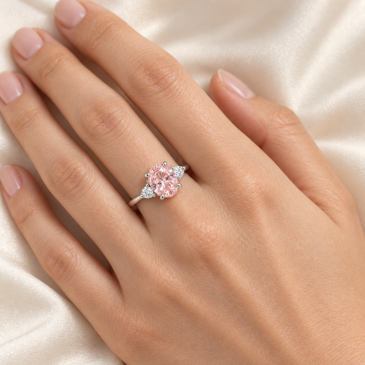 AI-generated on-hand design visualization of the Roselle soft oval pink lab-grown diamond ring with round white side stones in white-gold appearance; illustrative fit and scale.
