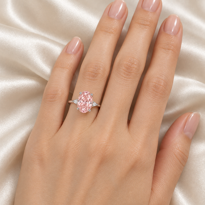 AI design visualization of the MISSISSI Rosewhisper oval pink lab-grown diamond ring worn on a model's left ring finger, with four claws, small round white shoulder accents and a slim white-metal band.