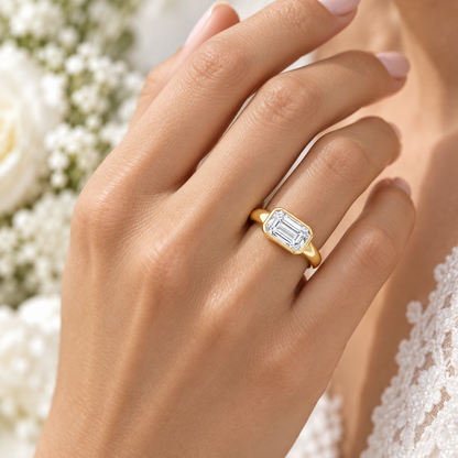 Serein east-west emerald-cut bezel engagement ring in 14K yellow gold, worn by a model.